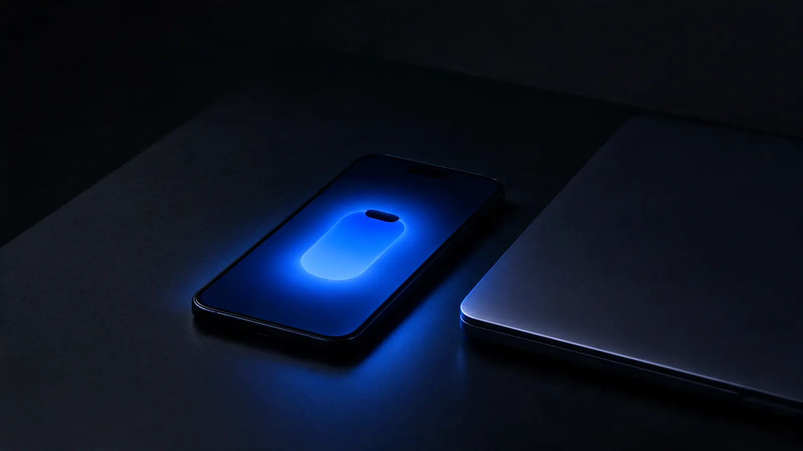 Celular deitado numa mesa escura, com a tela acesa em azul mostrando um alerta, ao lado de um notebook fechado