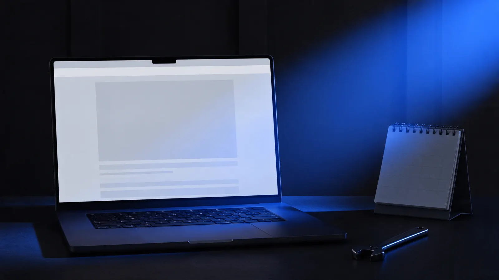 Notebook aberto numa mesa escura mostrando o esboço de um site, com um calendário de mesa e uma chave de boca ao lado, sob uma luz azul