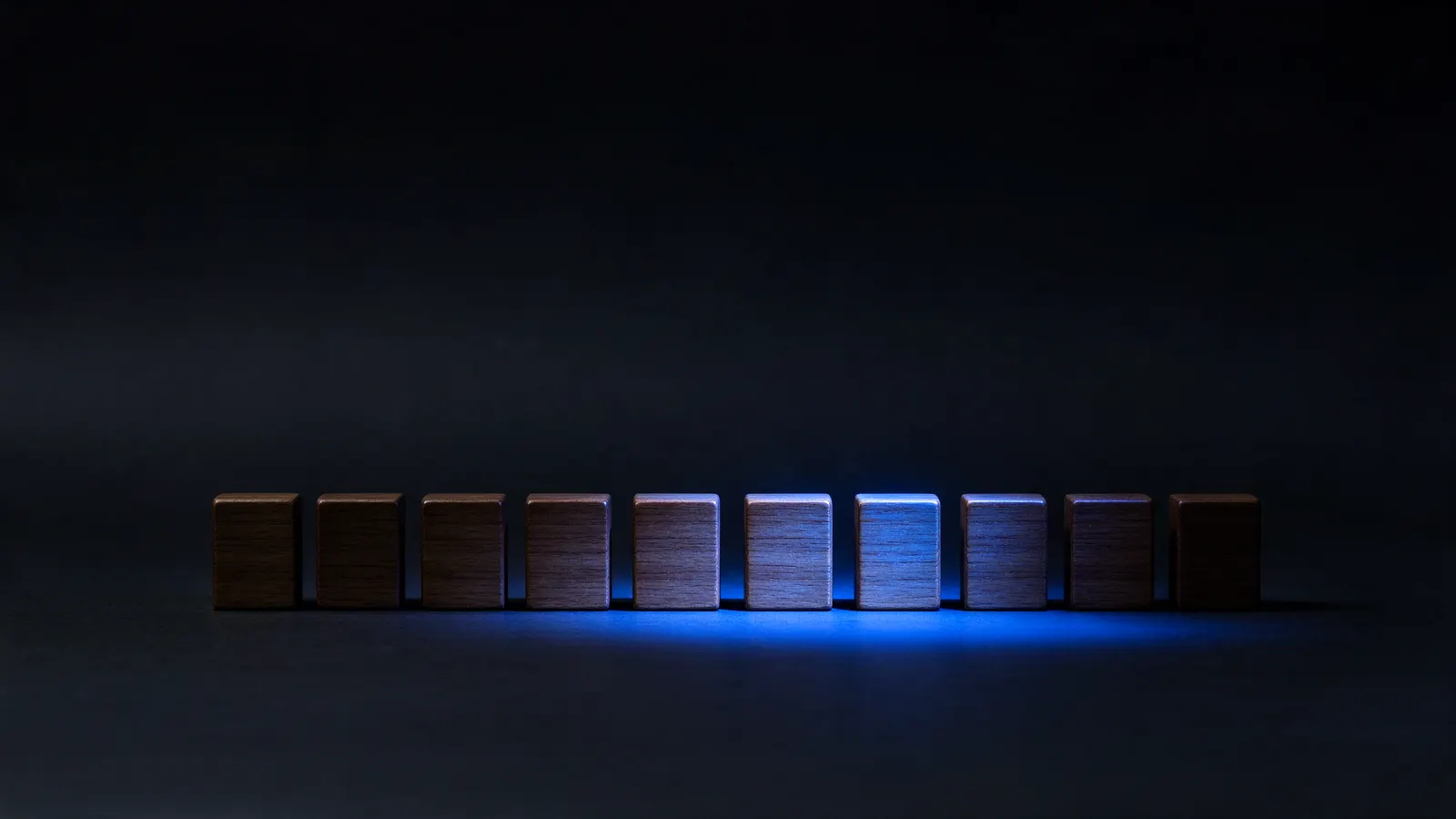 Fileira de dez blocos de madeira sobre uma mesa escura, com só os blocos do meio iluminados por uma luz azul