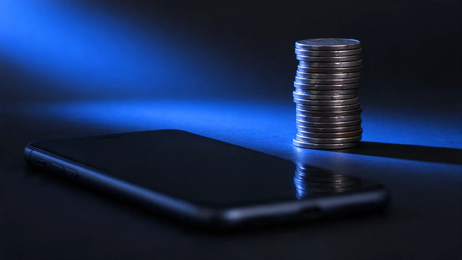Pilha de moedas ao lado de um celular numa mesa escura