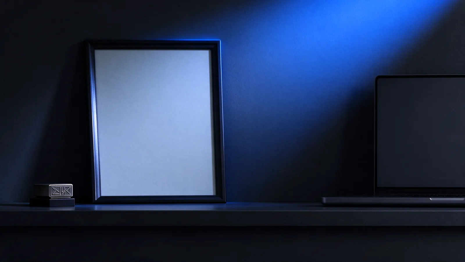 Frame with a blank certificate and a small stamp on a dark shelf, next to a laptop, under blue light